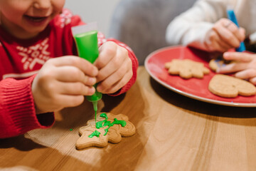 Cooking Christmas gingerbread. Child's hand decorating cookies tree with green confectionery mastic. Festive homemade decorated sweets. Friends making cookies icing view from above. Family culinary.
