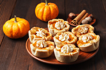 Naklejka na ściany i meble Pumpkin mini pies with whipped cream and spices on a wooden background