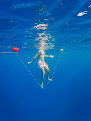Man standing on rope tied to buoys undersea