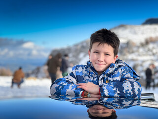 Smiling boy leaning on car roof against clear sky