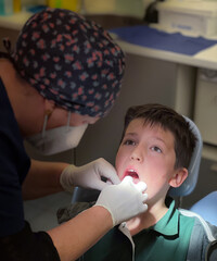 Dentist wearing floral cap examining boy's teeth