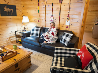 Woman with blanket relaxing on sofa in log cabin