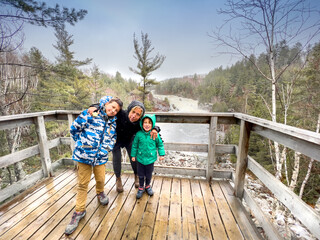 Portrait of mother with sons standing on wooden observation point against river and trees in woodland during vacation