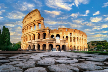 Naklejka na ściany i meble Colosseum at sunset in Rome, Italy. Low angle view of the main facade of the Colosseum and, in the foreground, the ancient paving in polished stone slabs.