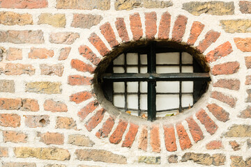 Little round window with cast iron fence in ancient brick wall, Utrecht, the Netherlands