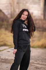 Portrait of a young beautiful cheerful dark-haired girl in a dark tracksuit.