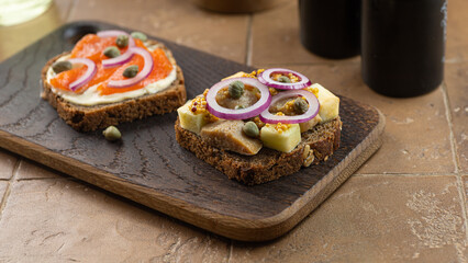 Toasts with dark rye bread, herring, pickled capers, salmon on black cutting board
