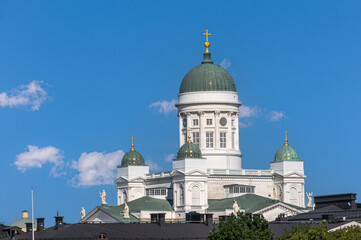Helsinki, Finland - July 20, 2022: The white Cathedral with green domes towers over black cityscape roofs under blue cloudscape