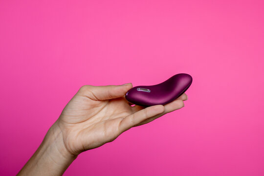 Hand with purple vibrating sex toy a pink background