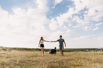 Fototapeta na wymiar Couple of man and woman walking in an open field with two dogs.