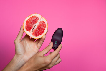 Hand with purple vibrating sex toy with grapefruit a pink background - obrazy, fototapety, plakaty