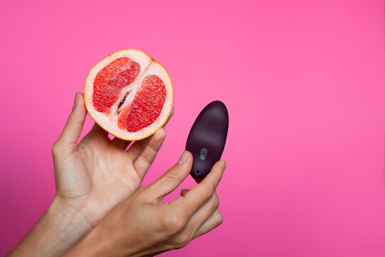 Hand with purple vibrating sex toy with grapefruit a pink background