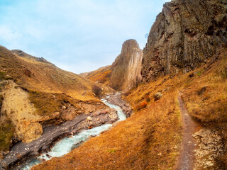 Beautiful autumn mountain landscape with bent mountain river. Bright alpine scenery with mountain river in red colors in fall time. Mountain trail along the slope above the stream. Caucasus Mountains