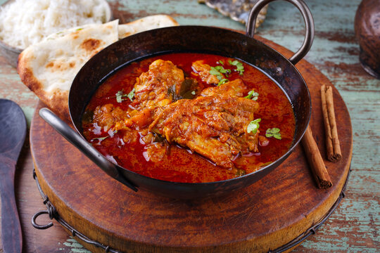 Traditional spicy Indian chicken Madras curry Rogan Josh with drumsticks, wings and garlic chapati bread served as close-up in a saucepan