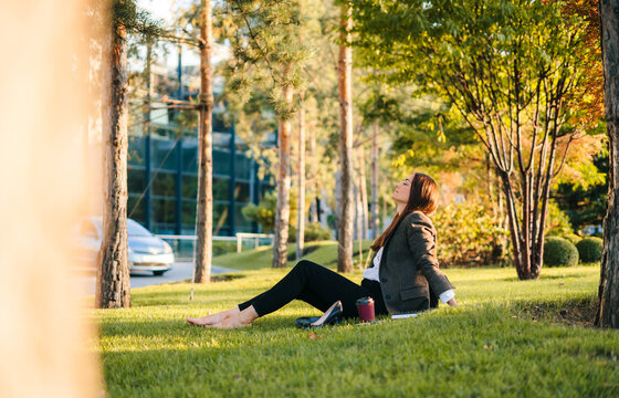 Side view of a calm business woman meditating, sitting in park after hard working day in office. Young beautiful woman enjoy in her free time. Leisure time
