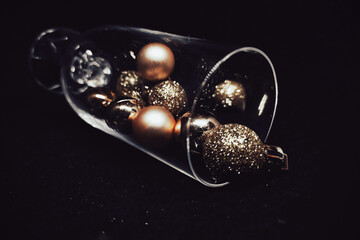 Golden Christmas tree balls in a  an overturned crystal transparent wine glass on a black background. Gold Christmas bauble as a decoration elements in crystal glass on dark background close-up