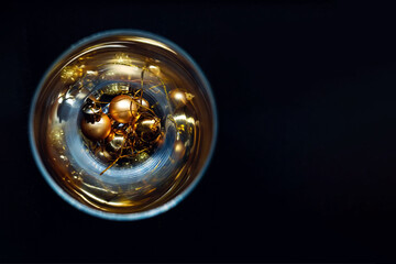 Black background with golden New year's decorations in a glass circle. Golden Christmas tree balls in circle glass goblet on a black background, top view
