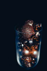 Gold shiny Christmas baubles decorations in a crystal goblet on a black background close-up. Golden Christmas balls decor elements in a glass on a dark background
