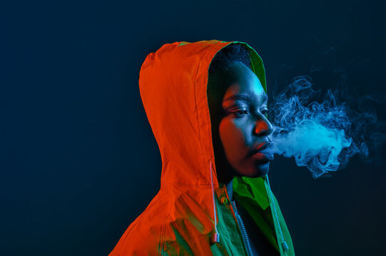 Hipster woman in raincoat blowing smoke from mouth