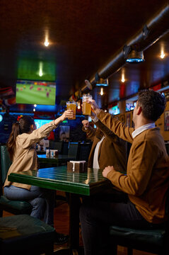 Friends watching football match clinking beer mug rest in sport bar