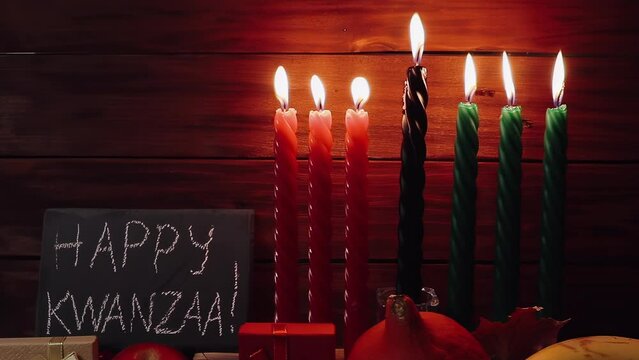 Kwanzaa African American holiday. Seven candles red, black and green on a natural wooden background. Congratulatory inscription and gifts. Symbols of African heritage.