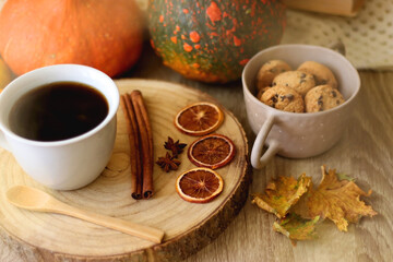 Cup of tea or coffee, seasonal spices, bowl of cookies, blanket, pumpkins, colorful leaves, books and tangerines on wooden table. Cozy hygge at home. Selective focus.