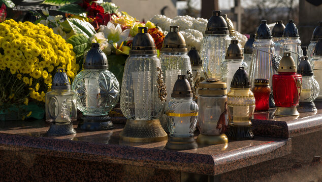 Dzień Wszystkich Świętych ( i Zaduszki) . Znicze płonące na grobie ( na cmentarzu parafialnym) pięknie udekorowanym kwiatami i wieńcami .