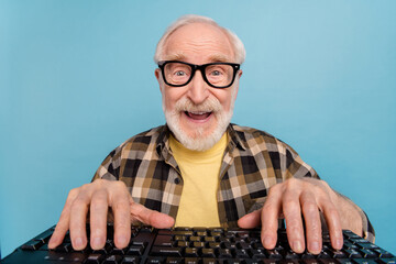 Photo of excited funny retired man wear plaid shirt spectacles typing modern device isolated blue...