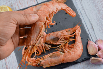 Close up raw shrimps over black stone plate with lemon and garlic for cuisine preparation