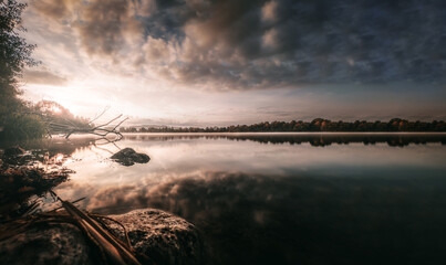 Obraz premium Sonnenaufgang am See mit vielen Reflektionen und einem dramatischen Wolken-Himmel