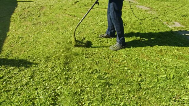 Faceless man in summer sandals mowing lawn with brush cutter. Leg, feet of male yardman in waterproof outdoor slippers who holds lawnmower. Gardener working on grassplot, backyard with grass trimmer