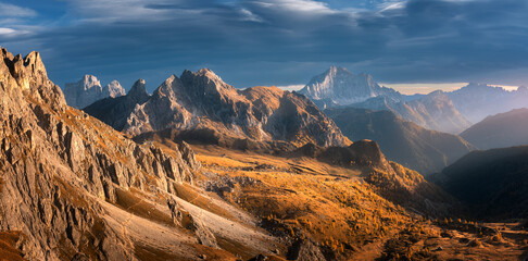 Beautiful mountains at sunset in autumn. Nature in Dolomites, Italy. Colorful panoramic landscape with rocks, orange grass and trees on hills, trail, dirt road, stones, blue sky with clouds in fall