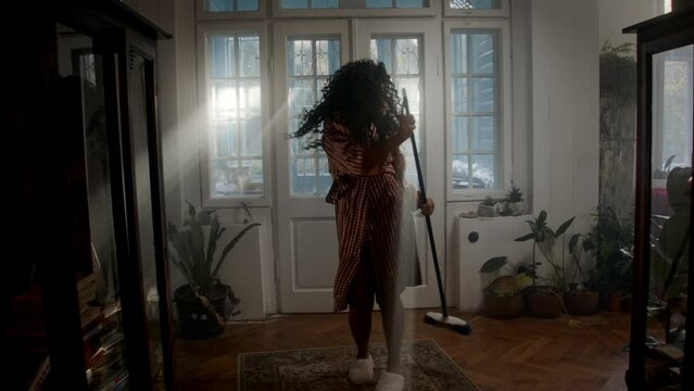 Black woman dancing with a brush in the corridor and being playful 