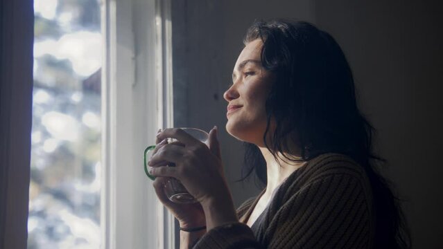 Woman drinking tea and looking out of window and smiling 
