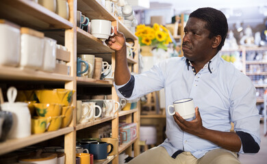 Focused african american man visiting household goods store in search of dishware, looking for new...