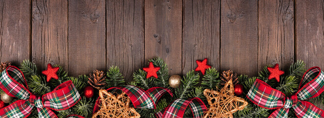 Christmas bottom border of ornaments, branches and red and green plaid bows and ribbon. Top view on...