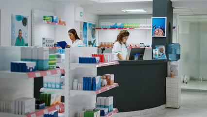 Diverse team of pharmacists working at drugstore counter to sell medicaments and pharmaceutics,...