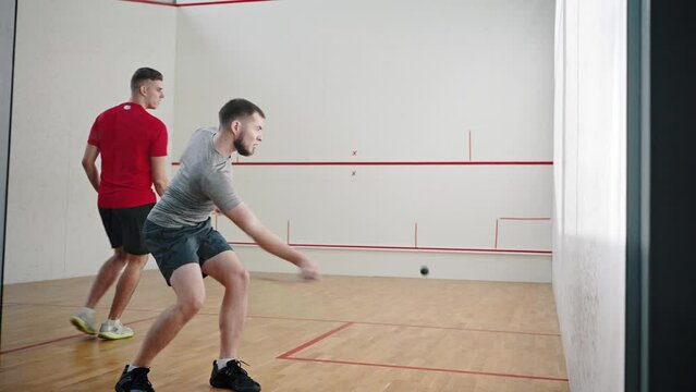 Couple of athletes plays squash in light court energetically