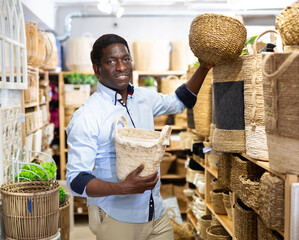Smiling African American looking for decorative wicker basket for storing household goods at store....