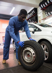 Fototapeta na wymiar Mechanic engaged in replacement of tyre on car wheel in auto workshop