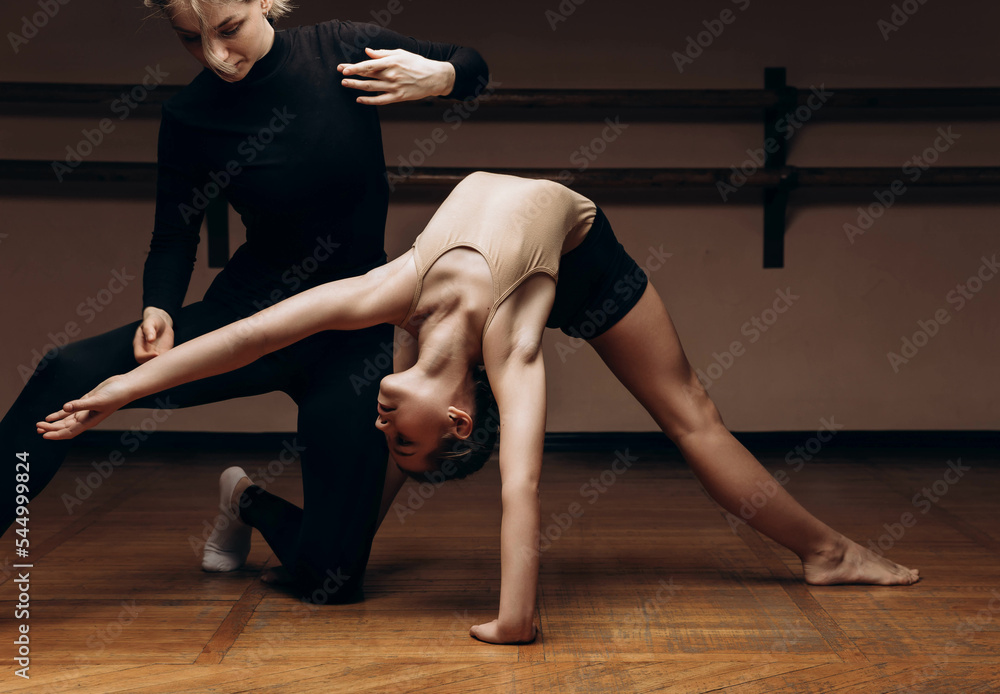 Wall mural Portrait of a choreographer's teacher helping a little girl to pose correctlyin a dance studio, dimmed light. place to copy