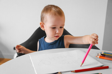 A child of 2 years old draws with colored pencils in an album. Child development. Creation.