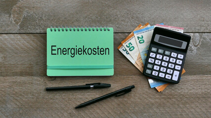 Notizblock mit dem Wort Energiekosten mit Eurobanknoten, Taschenrechner und Kugelschreiber.
