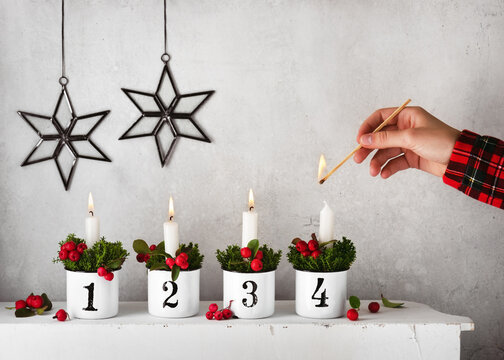 Girl hand lighting the fourth candle on a handmade advent wreath decorated with red checkerberries. Christmas home decoration concept. Copy space.