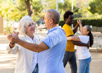 Smiling elderly woman enjoying dance with partner in garden