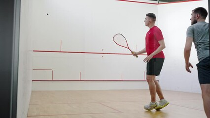 Young athletic men play squash in court hitting ball in turn