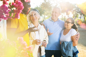 A group of mixed-race adult men and women of different age smiling and laughing while actively talking to each other outdoors 