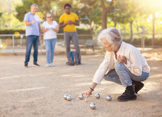 Smiling mature people playing petanque on sand together