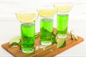 Sweet refreshing mint liqueur, with ice and mint leaves on table background, Shots with lime slice and mint flat lay