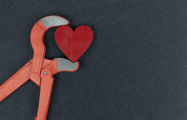 Red heart in jaws of a pipe wrench on black texture background.
Love danger Valentines. Health...